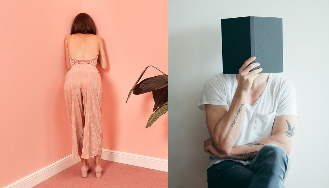 woman standing in corner of a room, man reading a book