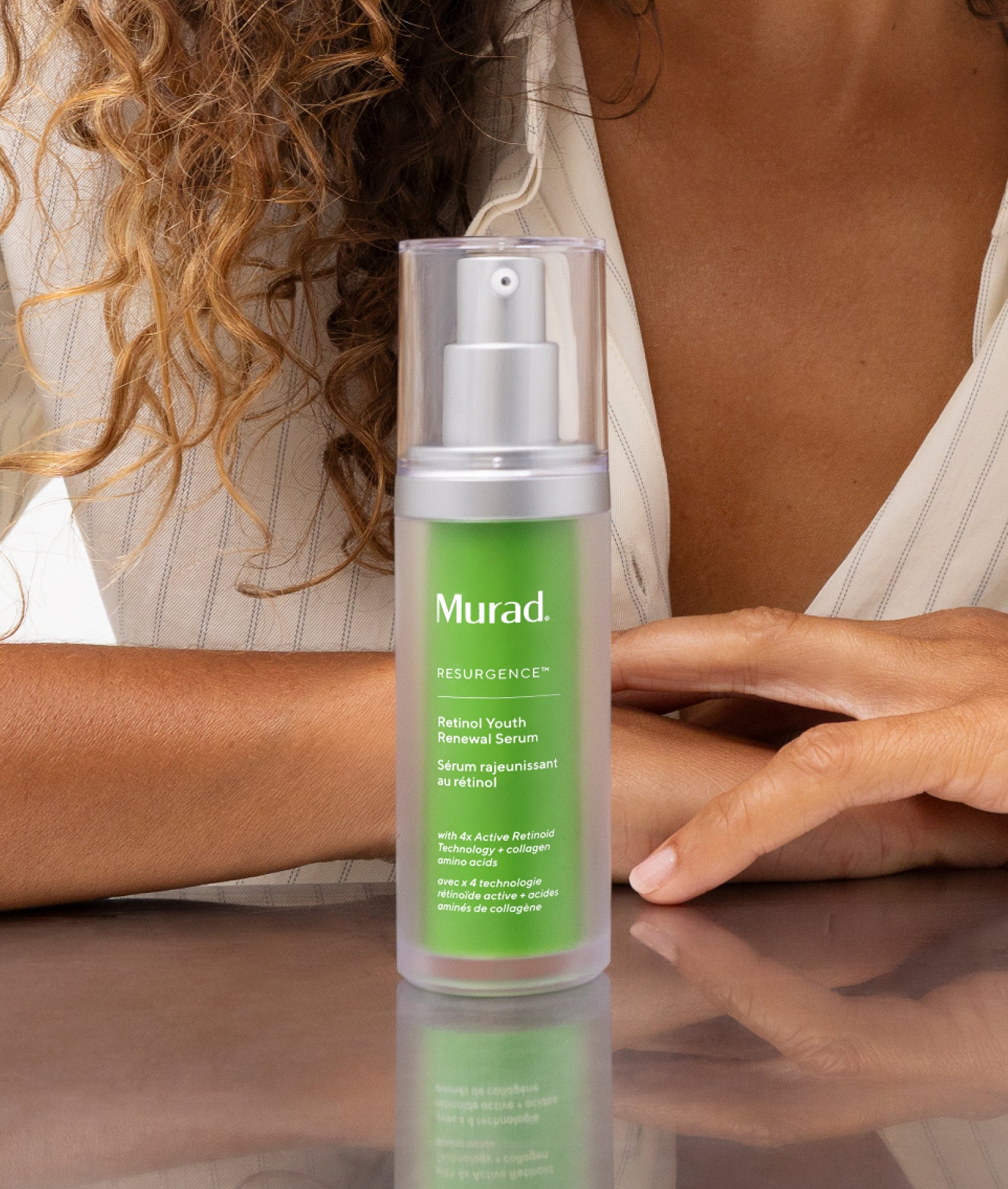 Murad Resurgence Natural Youth Renewal Serum in a clear bottle with a green label and silver pump, held in front of a woman in a white striped top.
