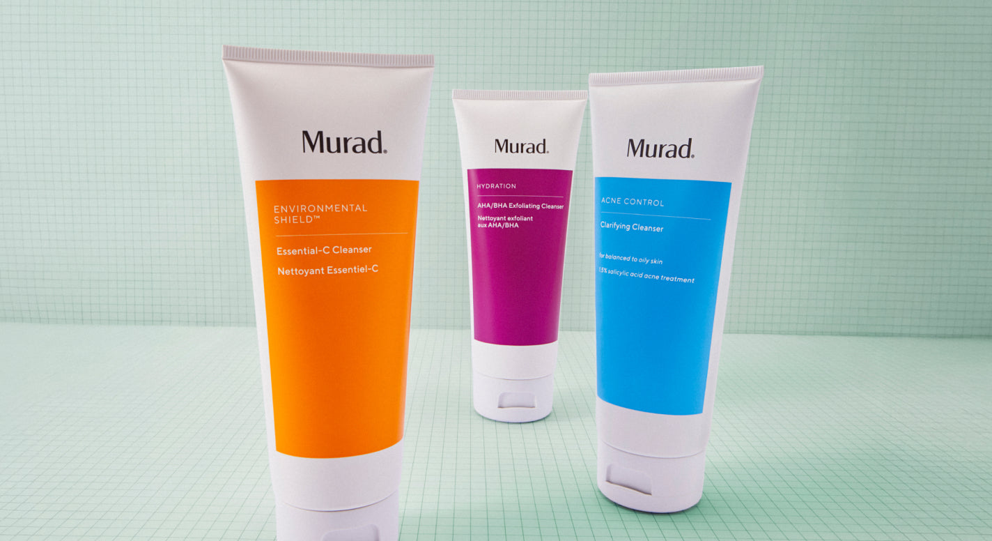 Three Murad skincare tubes standing upright on a pale mint green surface against a matching green grid-patterned backdrop. The left tube is orange, the center tube is magenta, and the right tube is blue, all with white caps and white upper bodies.