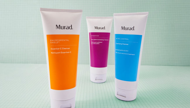 Three Murad skincare tubes standing upright on a light mint green surface against a matching mint green background. The left tube is orange and labeled Environmental Shield, the middle tube is purple and labeled Niacin, and the right tube is blue and labeled Acne Control.